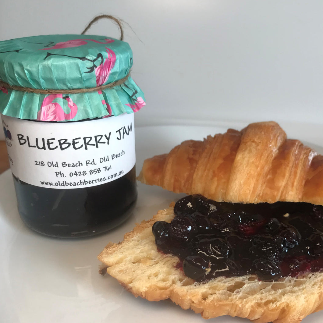 Jar of blueberry jam by Old Beach Berries alongside a fresh croissant spread with blueberry jam.